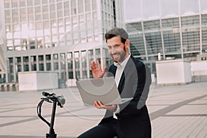 modern Successful man in a business suit outdoors near the scooter .Raises his hand up and rejoices in success looking