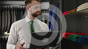 Modern suit shop good looking consultant using a laptop to check the stock of clothing and suits form the shop