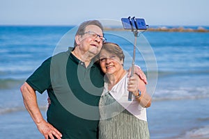 Modern sweet and loving hispanic mature couple taking selfie portrait- senior retired husband and wife on their 70s enjoying beach