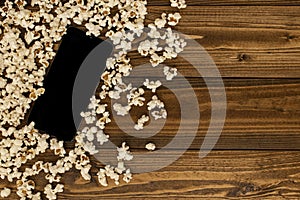 Modern tablet computer on wooden floor, black screen and blank, surrounded by popcorn. Besides copy space.