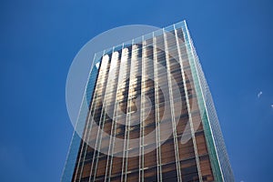 Modern tall building with glass facade against blue sky in sunny day. Office building of a company in an urban space