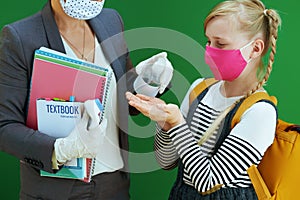 Modern teacher woman and school girl disinfecting hands