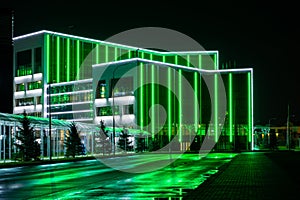 Modern tech building with neon green lines. A bewitching view with reflection of illumination on a wet road photo