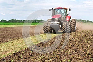 Modern tech red tractor plowing a green agricultural field in spring on the farm. Harvester sowing wheat.