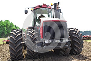 Modern tech red tractor plowing a green agricultural field in spring on the farm. Harvester sowing wheat.