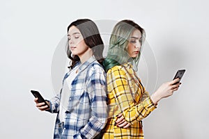 Modern technologies and internet addiction concept.Two young womans standing back to back, absorbed in electronic gadgets, not