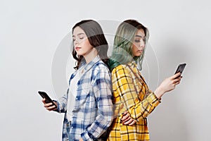 Modern technologies and internet addiction concept.Two young womans standing back to back, absorbed in electronic gadgets, not