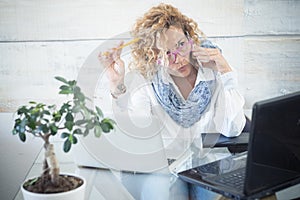 Modern technology job people - adult caucasian woman at office doing a phone call - laptop computer on the workplace desktop -