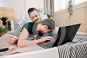 Modern technology. Pretty young gay couple using laptop while posing on bed and spending time together