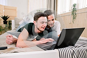 Modern technology. Pretty young gay couple using laptop while posing on bed and spending time together