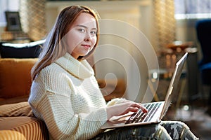 Modern teen girl with laptop sitting near couch