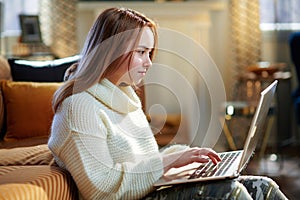 Modern teen girl surfing web while sitting near couch