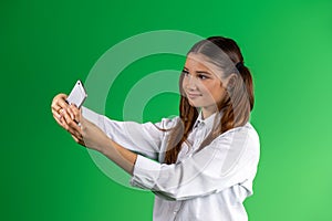 Modern teenage girl in school clothes, taking a selfie on a mobile phone. Green background