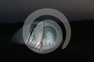 Modern tent lit from inside in wilderness at night. Overnight camping