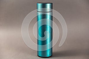 A modern thermos against a gray background. Cylindrical vacuole flask in turquoise color. Container for hot and cold drinks.