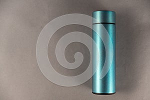 A modern thermos against a gray background. Cylindrical vacuole flask in turquoise color. Container for hot and cold drinks.