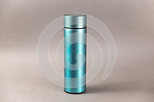 A modern thermos against a gray background. Cylindrical vacuole flask in turquoise color. Container for hot and cold drinks.