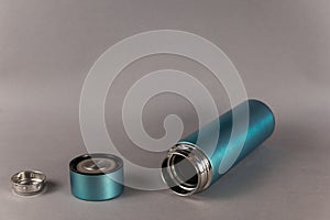 Modern thermos, lid and teapot against a gray background. Cylindrical vacuole flask in turquoise color. Container for hot and cold