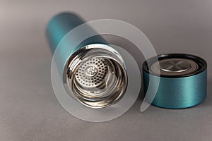A modern thermos with an open lid lies against a gray background. Cylindrical vacuole flask in turquoise color. Container for hot
