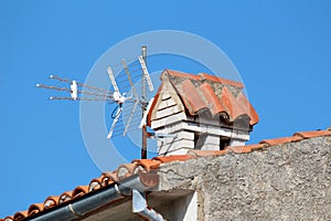 Modern three way TV antenna mounted on partially rusted metal pipe next to white brick chimney on top of family house