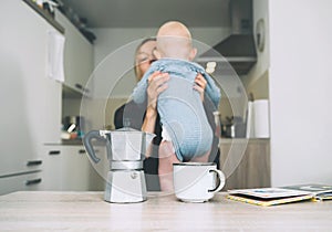 Modern tired mother and little child after sleepless night. Exhausted woman with baby is sitting with coffee in kitchen. Life of