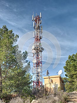 Modern tower with huge complex of telecommunication antennas on old bricks house hidden in pine trees.  Mountain trail over Pintal photo