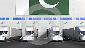 Modern trailer trucks load or unload at warehouse bays with flag of Pakistan. Pakistani logistics related conceptual 3D
