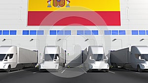 Modern trailer trucks load or unload at warehouse bays with flag of SPAIN. Spanish logistics related conceptual 3D