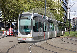 Modern tram traveling through city urban environment along tramlines in the sunshine