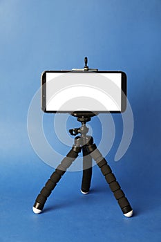 Modern tripod with smartphone on blue background