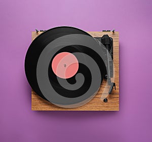 Modern turntable with vinyl record on purple background, top view