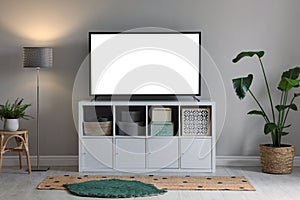 Modern TV on cabinet, floor lamp and beautiful houseplants near light wall indoors. Interior design