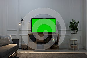 Modern TV on cabinet, floor lamp and houseplants near light wall indoors. Interior design