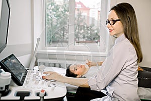 Modern ultrasound device in medical center. Young woman doctor makes examination of the thyroid gland for her female