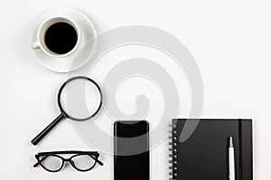 Modern unisex working space, top view. Notepad, pen, coffee, smartphone, magnifier, glasses on white background, copy space, flat