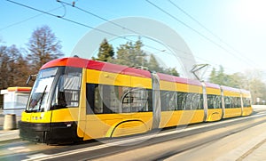 Modern urban rail transport. Yellow tram with motion blur effect moves fast in the city. High speed passenger train in motion on