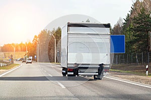 A modern van with a tail lift is driving along an asphalt road against the backdrop of a sunset. Concept of road