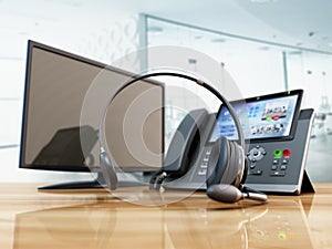 Modern VoIP phone and headset standing on wooden office table. Call center, marketing and technical support concept. 3D