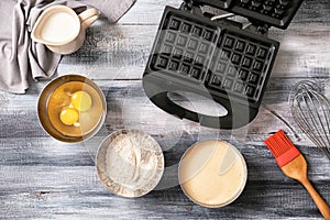 Modern waffle maker with ingredients on wooden table