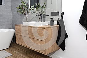 A modern washbasin in the bathroom in a wall-mounted cabinet with a matte black faucet, a visible mirror and artificial flowers.