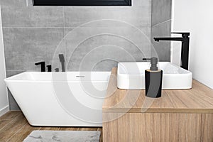 A modern washbasin in the bathroom in a wall mounted cupboard with a matte black faucet, a wall lined with gray ceramic tiles.