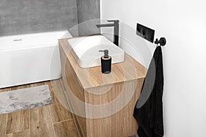 A modern washbasin in the bathroom in a wall mounted cupboard with a matte black faucet, a wall lined with gray ceramic tiles.