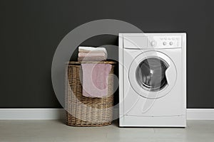 Modern washing machine and laundry basket near black wall