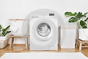 Modern washing machine, laundry in baskets and domestic room interior