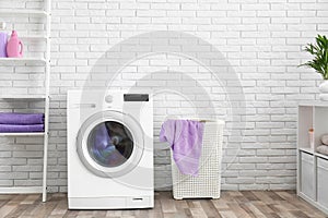 Modern washing machine near brick wall in laundry room interior