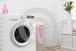 Modern washing machine near brick wall in laundry room interior