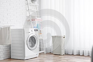 Modern washing machine near brick wall in laundry room interior