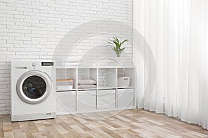 Modern washing machine near brick wall in laundry room interior