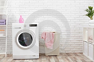 Modern washing machine near brick wall in laundry room interior