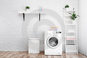 Modern washing machine near brick wall in laundry room interior